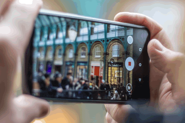 A person taking a photo of a busy indoor marketplace with a smartphone, capturing people and colorful storefronts, showcasing the vibrant atmosphere for a social media planner | plannthat.com