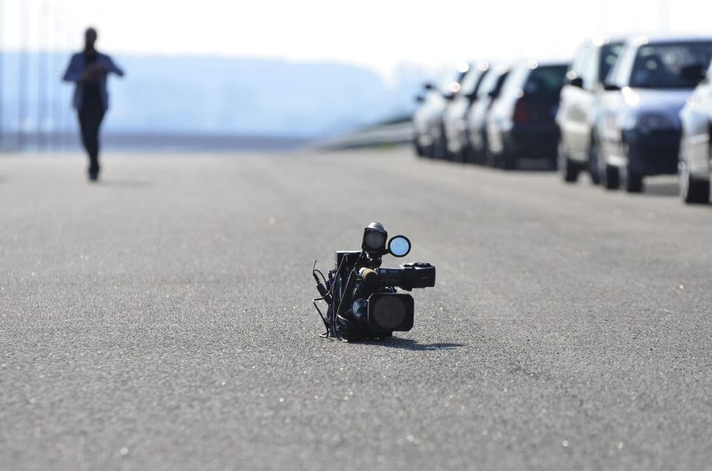 A video camera lies on an empty road with a row of parked cars on the right and a blurred person approaching from the distance, illustrating the use of an Instagram scheduler for capturing content | plannthat.com