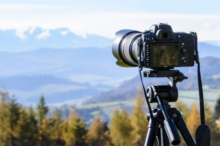 A DSLR camera on a tripod capturing a scenic landscape with mountains and forests in the background, perfect for a social media planner | plannthat.com