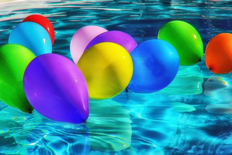 Colorful balloons floating on a clear blue swimming pool, reflecting vibrant hues of red, blue, green, purple, and yellow. The shimmering water enhances the festive and cheerful atmosphere, perfect for a social media planner | plannthat.com