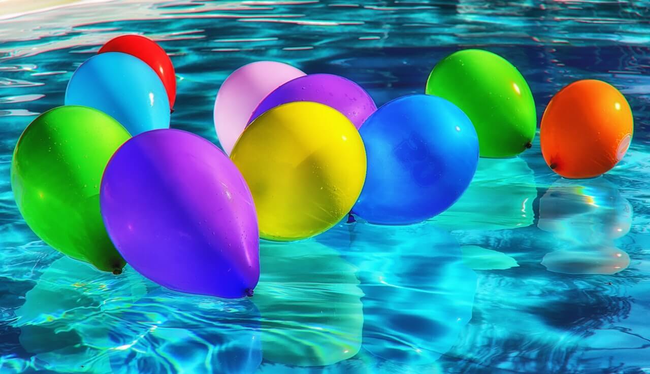 Colorful balloons floating on a clear blue swimming pool, reflecting vibrant hues of red, blue, green, purple, and yellow. The shimmering water enhances the festive and cheerful atmosphere, perfect for a social media planner | plannthat.com