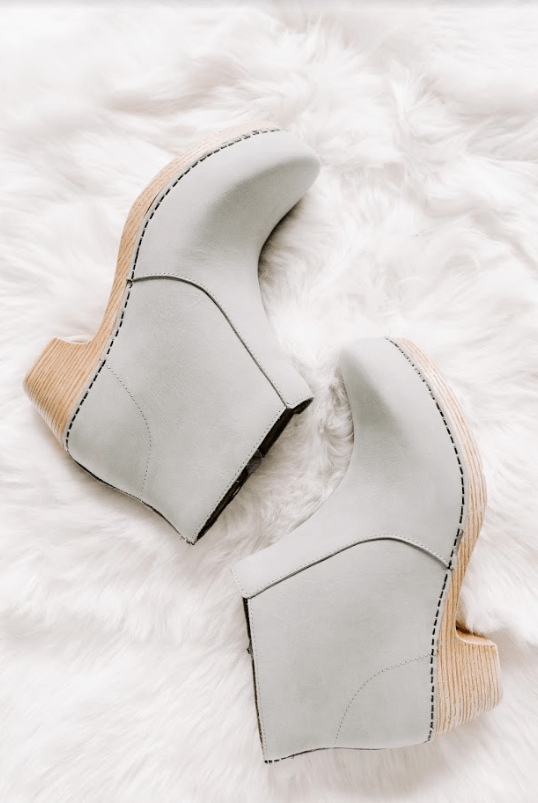 A pair of light gray, high-heeled ankle boots with wooden soles on a fluffy white surface, showcasing their stylish design and craftsmanship, featuring visible stitching and a sleek, modern look, perfect for your Instagram scheduler | plannthat.com