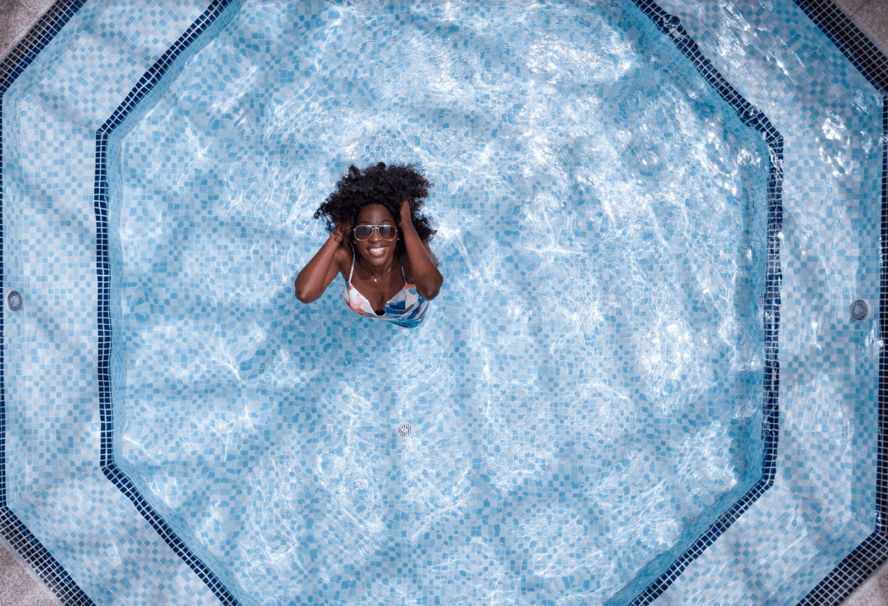 A woman wearing sunglasses and a swimsuit enjoys herself in a tiled swimming pool, viewed from above, perfect for showcasing a relaxing moment on your Instagram scheduler | plannthat.com