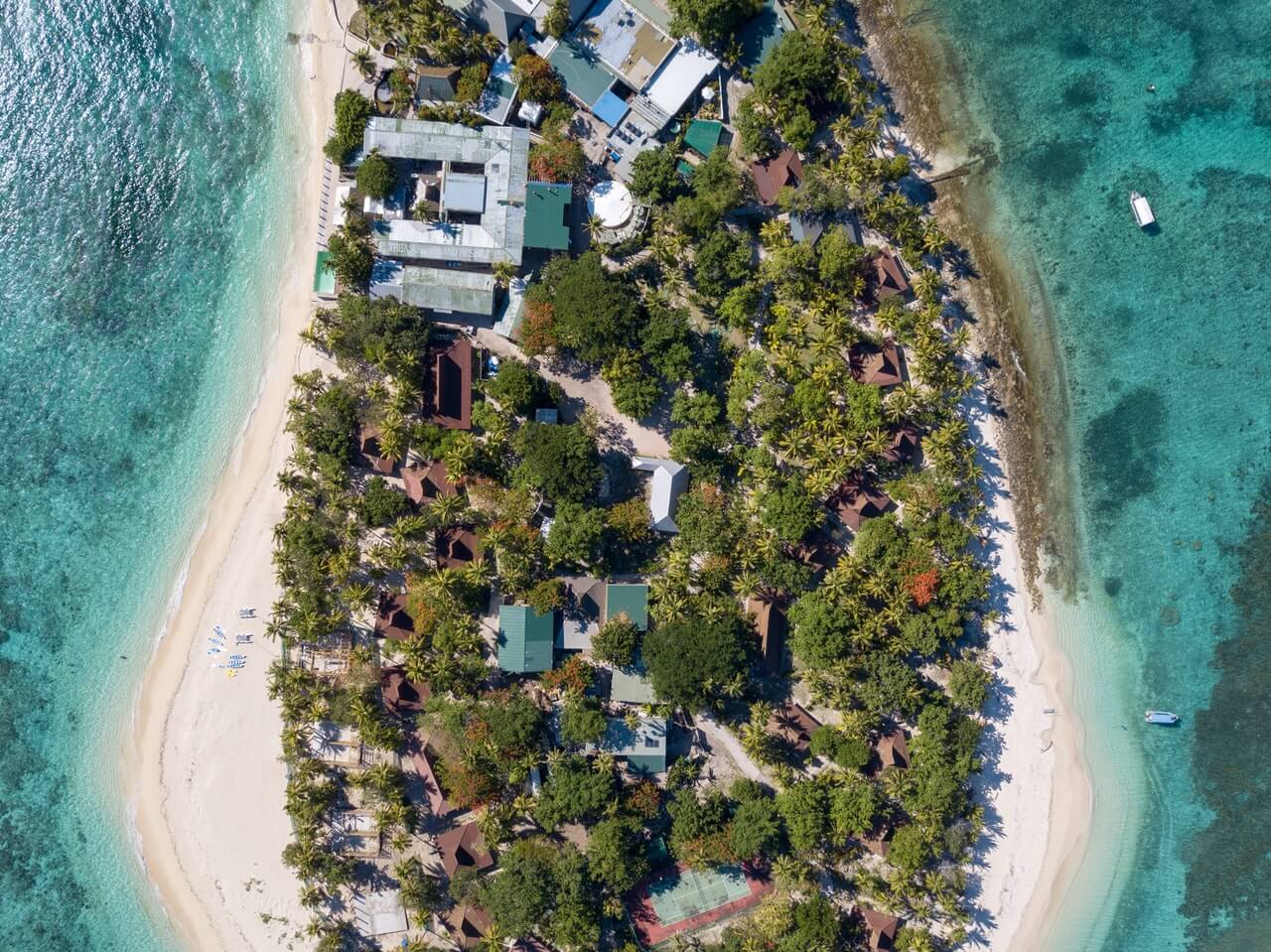 Aerial view of a tropical island with lush greenery, buildings, and surrounding turquoise waters. Sandy beaches encircle the island, and a small boat is visible near the shore, showcasing a serene and picturesque island destination, perfect for an Instagram scheduler. | plannthat.com