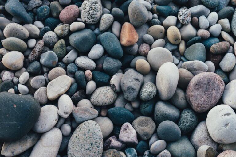 Assorted smooth pebbles of various sizes and colors, including shades of grey, blue, and beige, closely packed together, resembling the organized approach of a social media scheduler | plannthat.com
