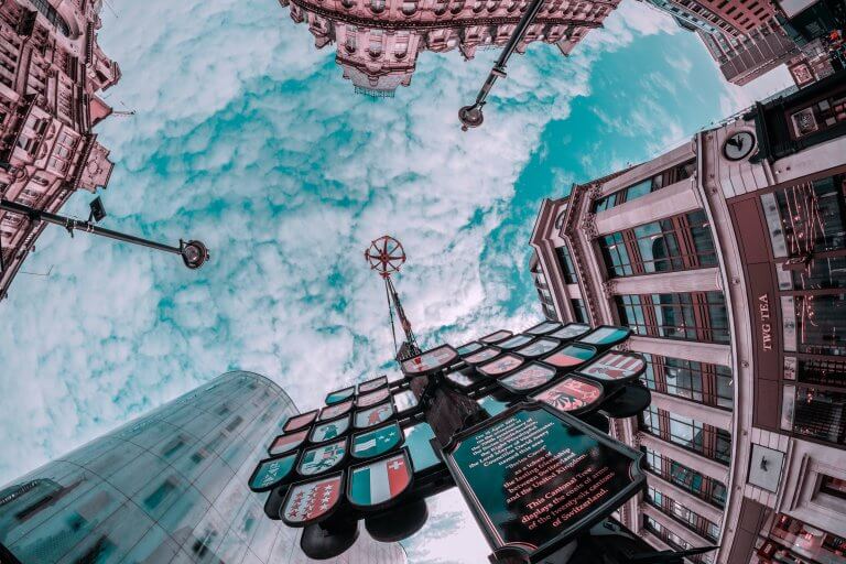 Upward view of a city intersection with historic buildings, a signpost displaying various flags, street lamps, and a cloudy blue sky, perfect for showcasing on a social media scheduler | plannthat.com