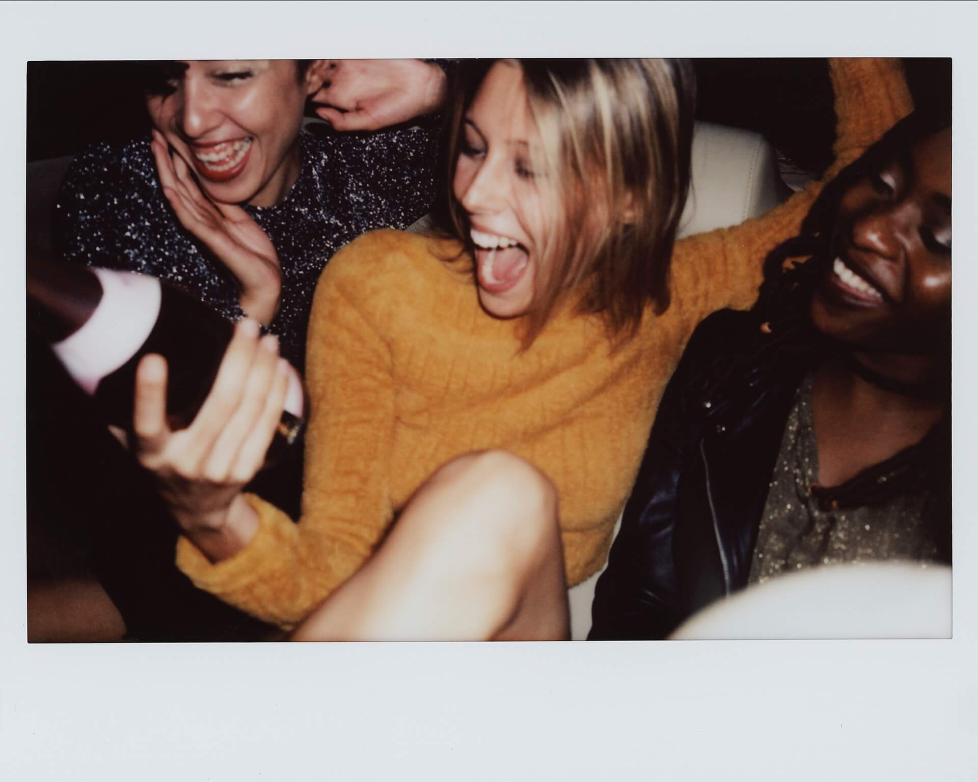 Three women joyfully celebrating with one holding a bottle of champagne, laughing and having a great time together, suggesting a fun social gathering or party, perfect for showcasing moments with a social media planner | plannthat.com
