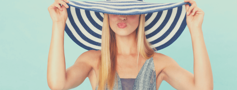 A woman with long blonde hair playfully holds a wide-brimmed, striped hat over her eyes, making a kissing face against a light blue background, showcasing a fun moment perfect for your Instagram scheduler | plannthat.com