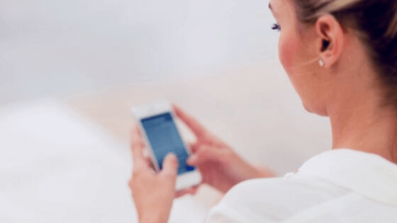 A person with blonde hair is seen from behind, holding and using a smartphone, likely engaging with a social media scheduler | plannthat.com
