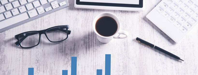 Office desk with glasses, coffee cup, pen, keyboard, tablet, and calculator on a light wooden surface, featuring a bar graph overlay | Social media scheduler | plannthat.com