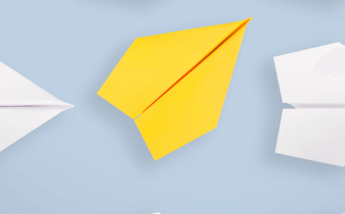 A yellow paper airplane stands out against a light blue background surrounded by white paper airplanes, symbolizing creativity and uniqueness | Social media scheduler | plannthat.com