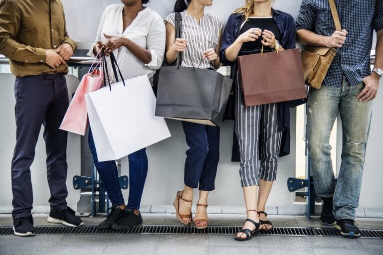 A group of people standing and holding shopping bags, suggesting they have been shopping, only their torsos and legs are visible, during Black Friday sales | plannthat.com