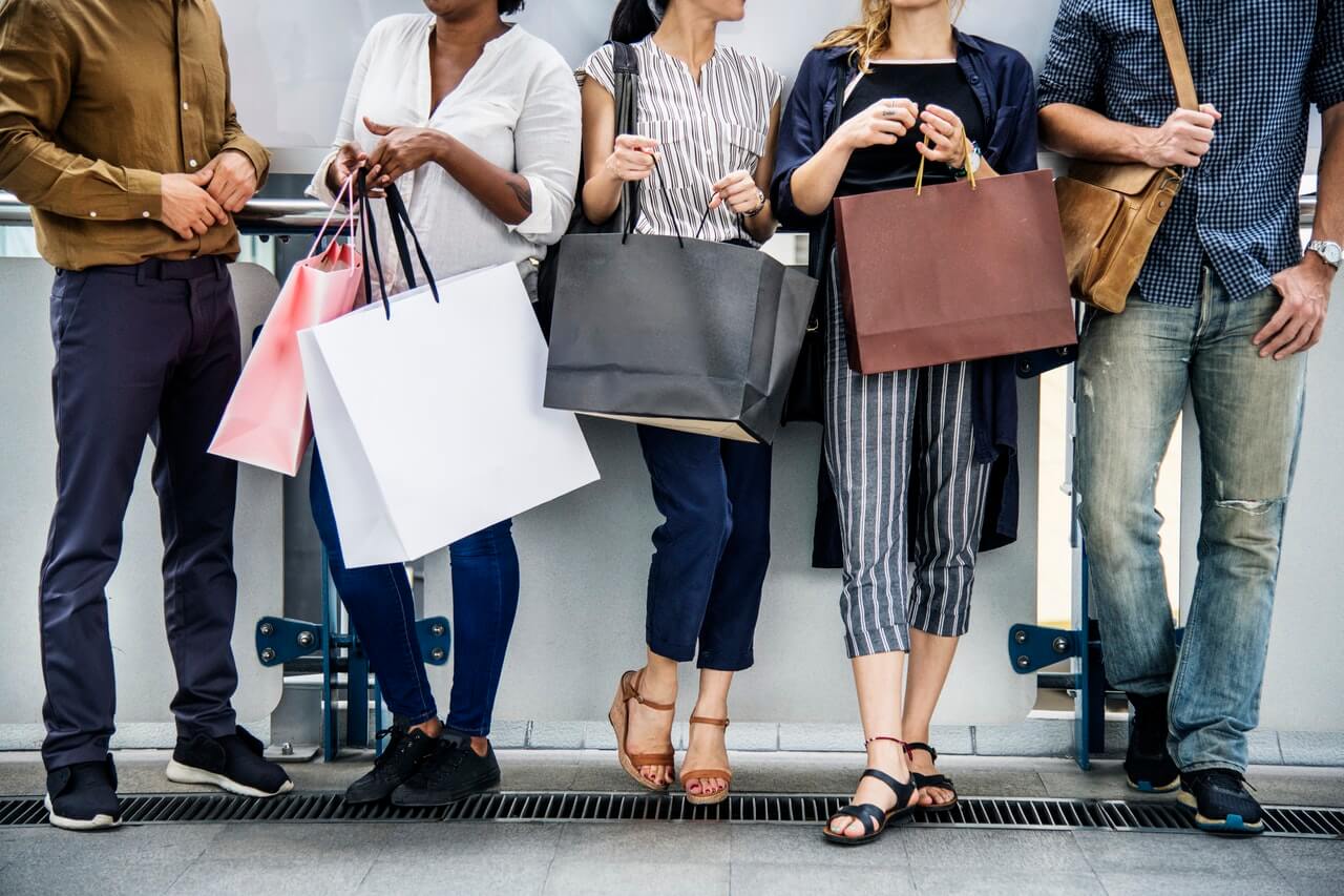 A group of people standing and holding shopping bags, suggesting they have been shopping, only their torsos and legs are visible, during Black Friday sales | plannthat.com