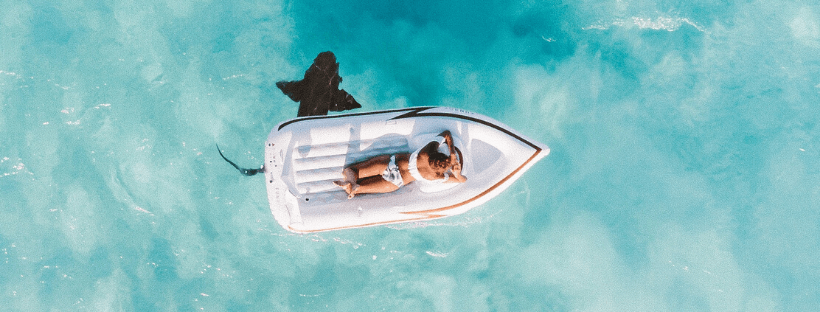 A person relaxes on an inflatable boat in clear blue water, with a shark swimming nearby, aerial view, perfect for showcasing your Instagram scheduler | plannthat.com