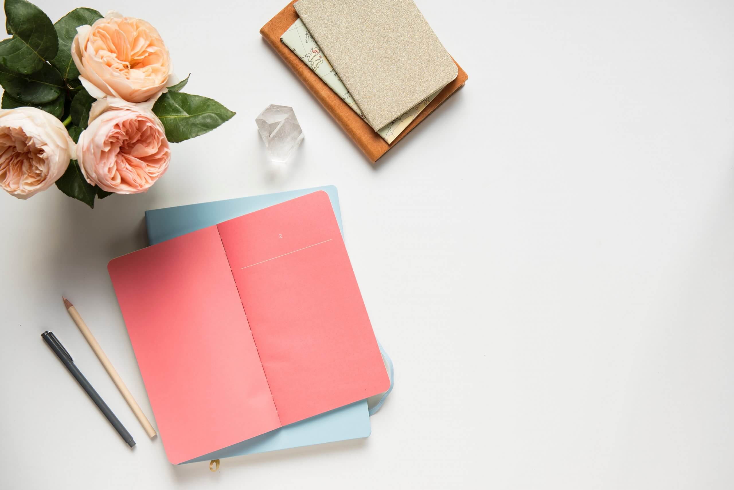 Open red notebook on a white desk with a pencil, pen, flowers, and stacked books, ideal for a social media planner | plannthat.com