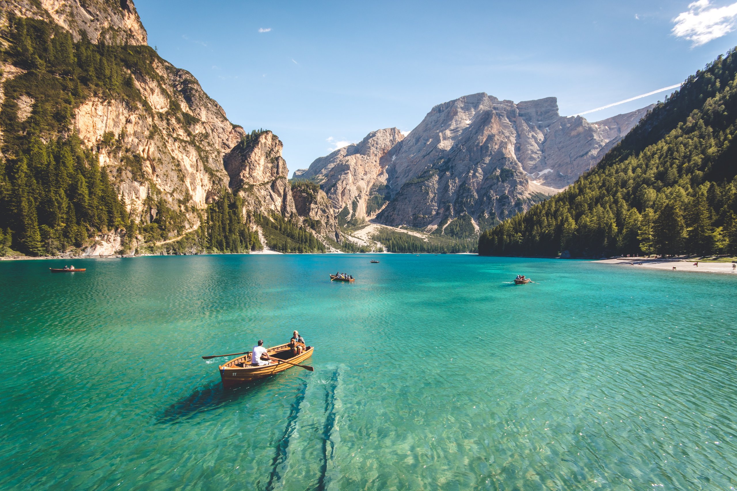 A serene lake surrounded by majestic mountains with clear turquoise water, several wooden boats with people floating on the lake, enjoying the picturesque landscape under a bright blue sky, dense forests line the shore in the background, perfect for capturing moments with an Instagram scheduler | plannthat.com