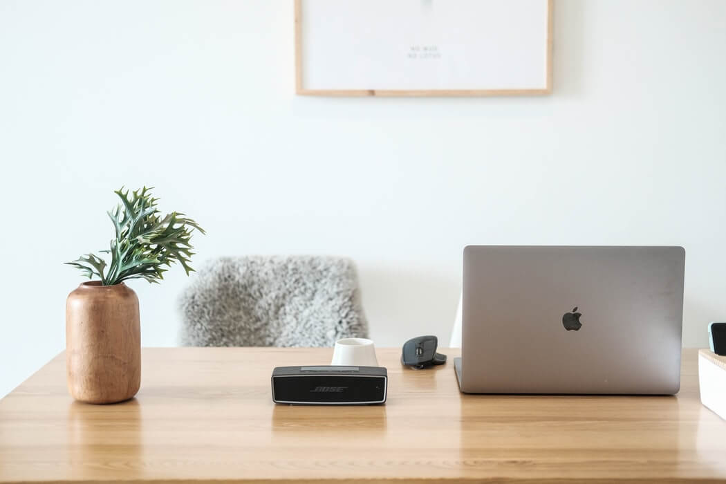 A minimalistic desk setup with a laptop, a black speaker, a potted plant, a mouse, and a coffee cup on a wooden table, perfect for using a social media scheduler | plannthat.com