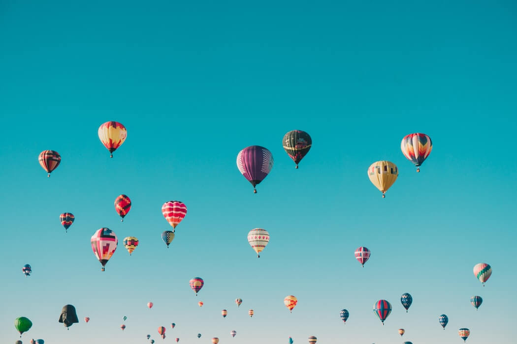 A clear blue sky filled with numerous colorful hot air balloons of various patterns and designs, floating at different heights, creating a vibrant and picturesque scene, evoking a sense of adventure and freedom, perfect for sharing on your Instagram scheduler | plannthat.com
