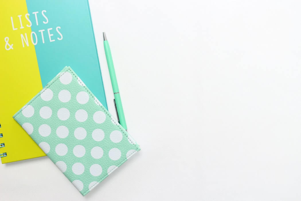 A colorful notebook labeled "Lists & Notes," a mint green polka dot wallet, and a matching mint green pen neatly arranged on a white surface, creating a bright and organized workspace for a social media planner | plannthat.com