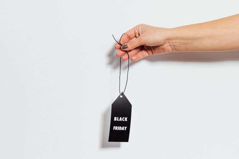 A hand holding a black tag with "Black Friday" written on it, against a plain white background, perfect for promoting deals with a social media scheduler | plannthat.com