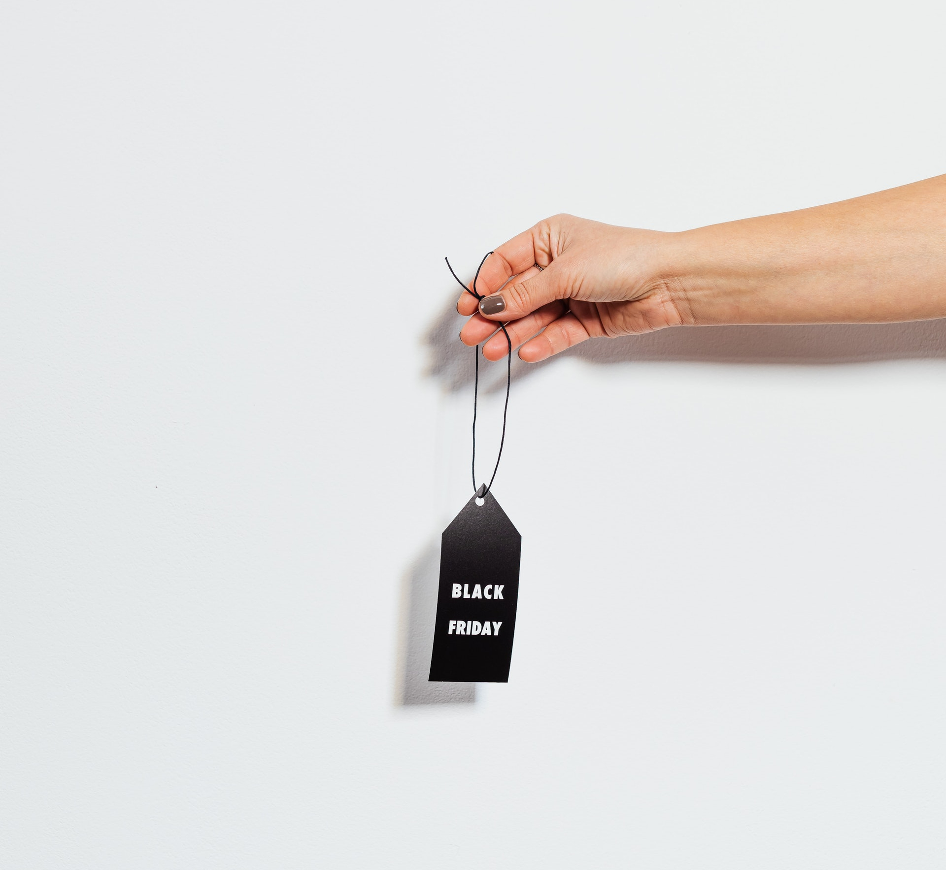 A hand holding a black tag with "Black Friday" written on it, against a plain white background, perfect for promoting deals with a social media scheduler | plannthat.com