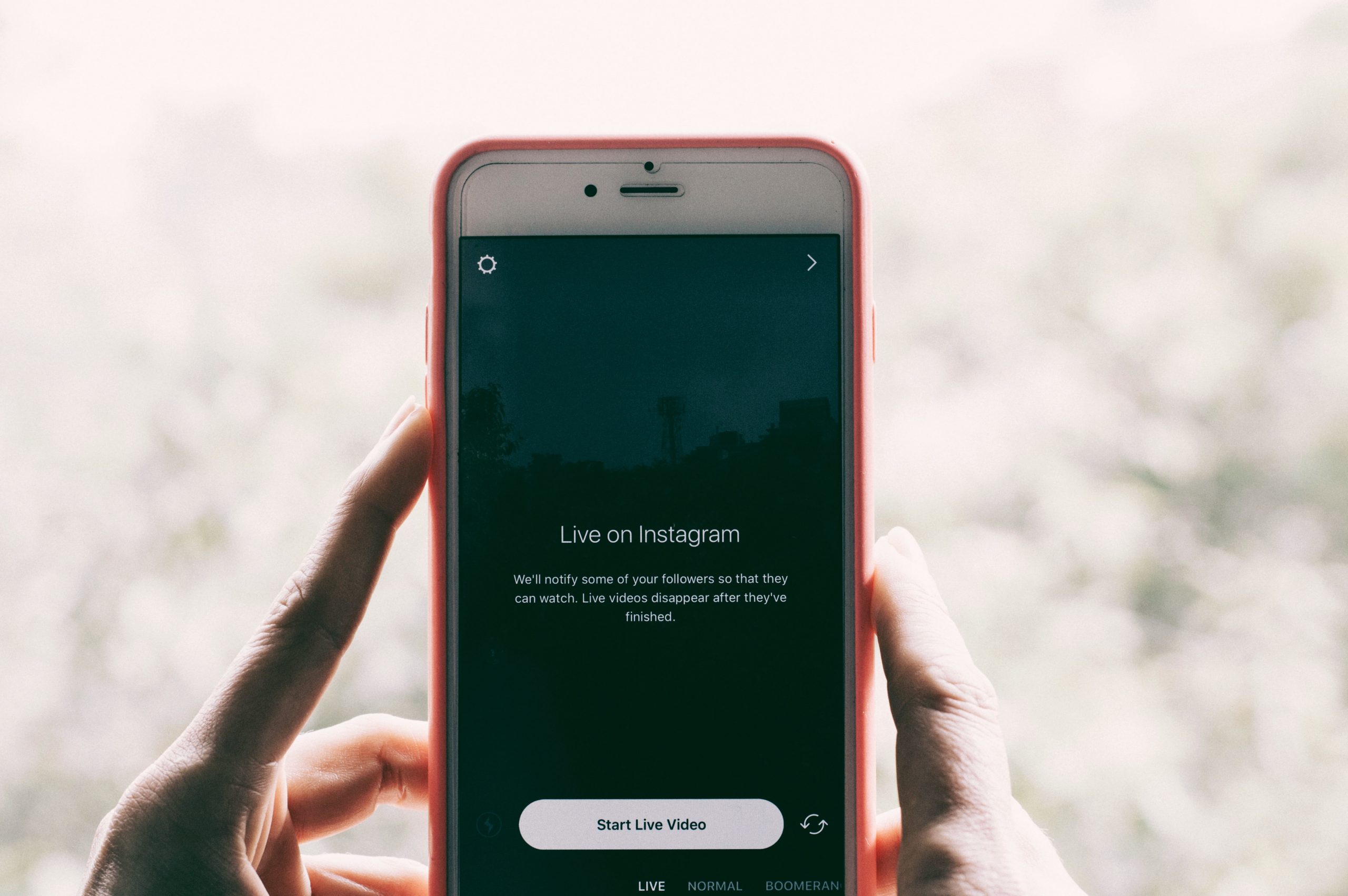 Person holding a smartphone with the Instagram app open, preparing to start a live video. The phone screen displays "Live on Instagram" with an option to "Start Live Video." | plannthat.com