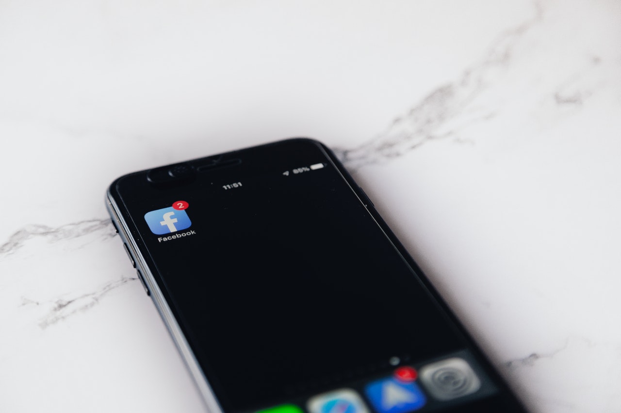 Smartphone displaying Facebook app icon with two notifications on marble surface, other app icons visible at bottom | Social media planner | plannthat.com