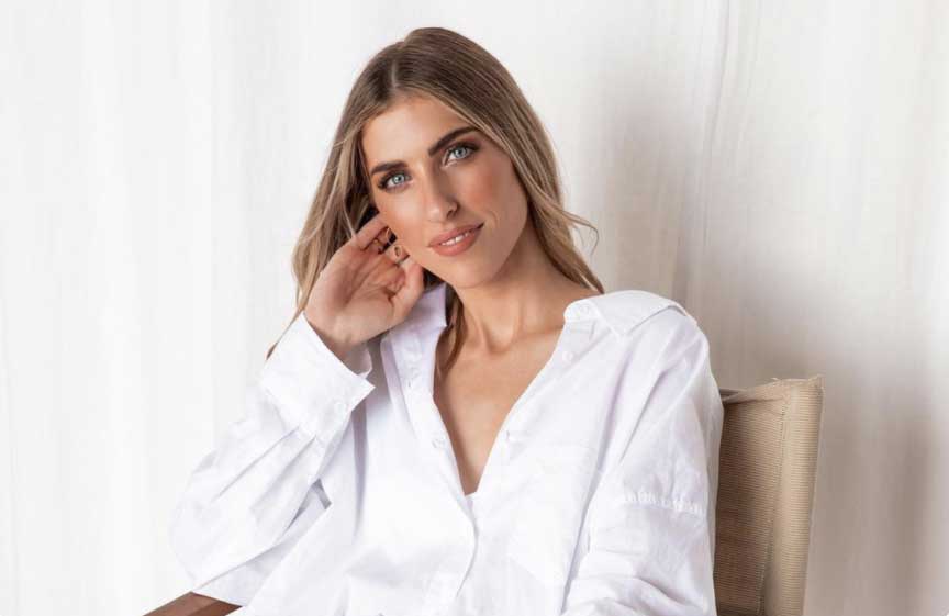 A woman with long hair wearing a white shirt is seated, resting her head on her hand, and smiling softly against a light background, illustrating a relaxed moment ideal for a social media planner | plannthat.com A woman with long hair wearing a white shirt is seated, resting her head on her hand, and smiling softly against a light background, illustrating a relaxed moment ideal for a social media planner | plannthat.com