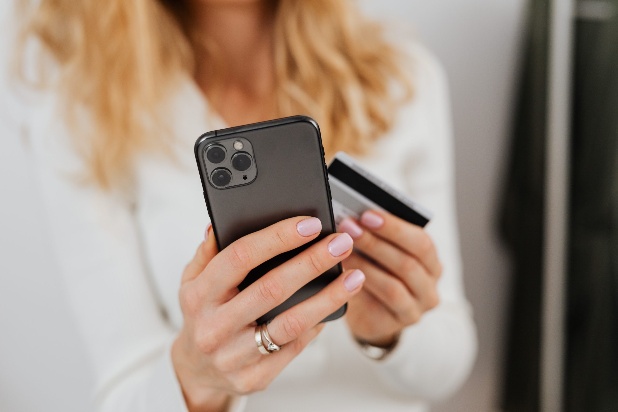 A person holding a smartphone and a credit card, possibly making an online purchase, with a focus on the hands and the devices, illustrating the convenience of using a social media scheduler | plannthat.com