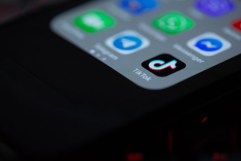 Close-up of a smartphone screen displaying various app icons, with the TikTok app prominently featured in the center, slightly tilted against a dark background, emphasizing the illuminated icons, ideal for a social media planner | plannthat.com