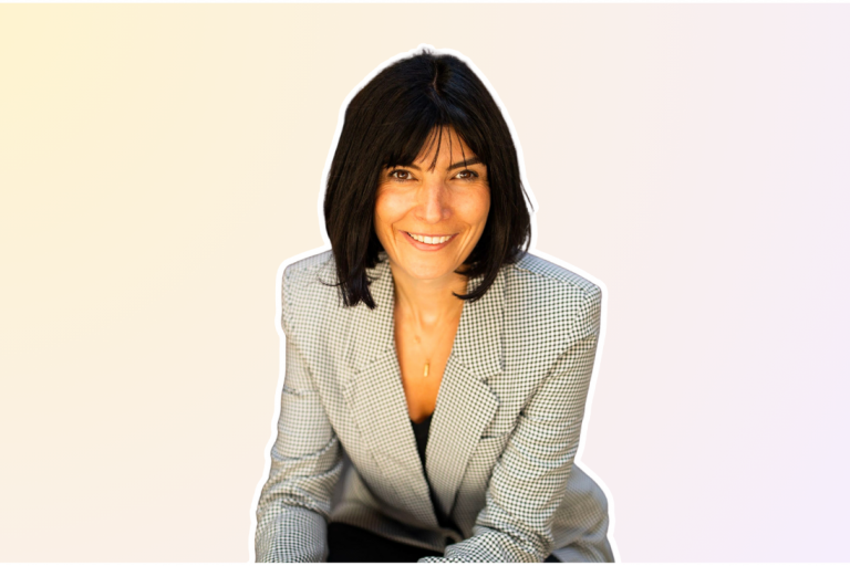 A woman with shoulder-length dark hair smiles while wearing a light gray checkered blazer over a black top, exuding a professional and approachable demeanor | Social media planner | plannthat.com