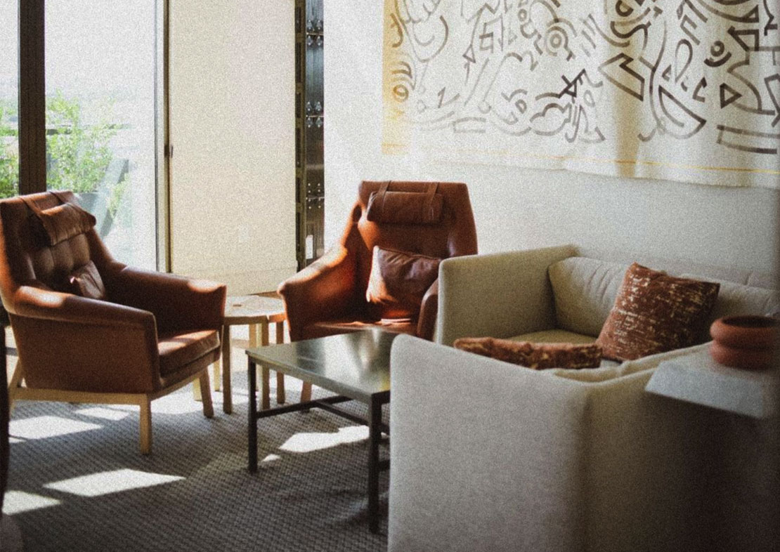 A cozy living room with brown leather chairs, a cream sofa, a coffee table, and abstract wall art, illuminated by natural light streaming through a glass door, perfect for planning your social media scheduler | plannthat.com
