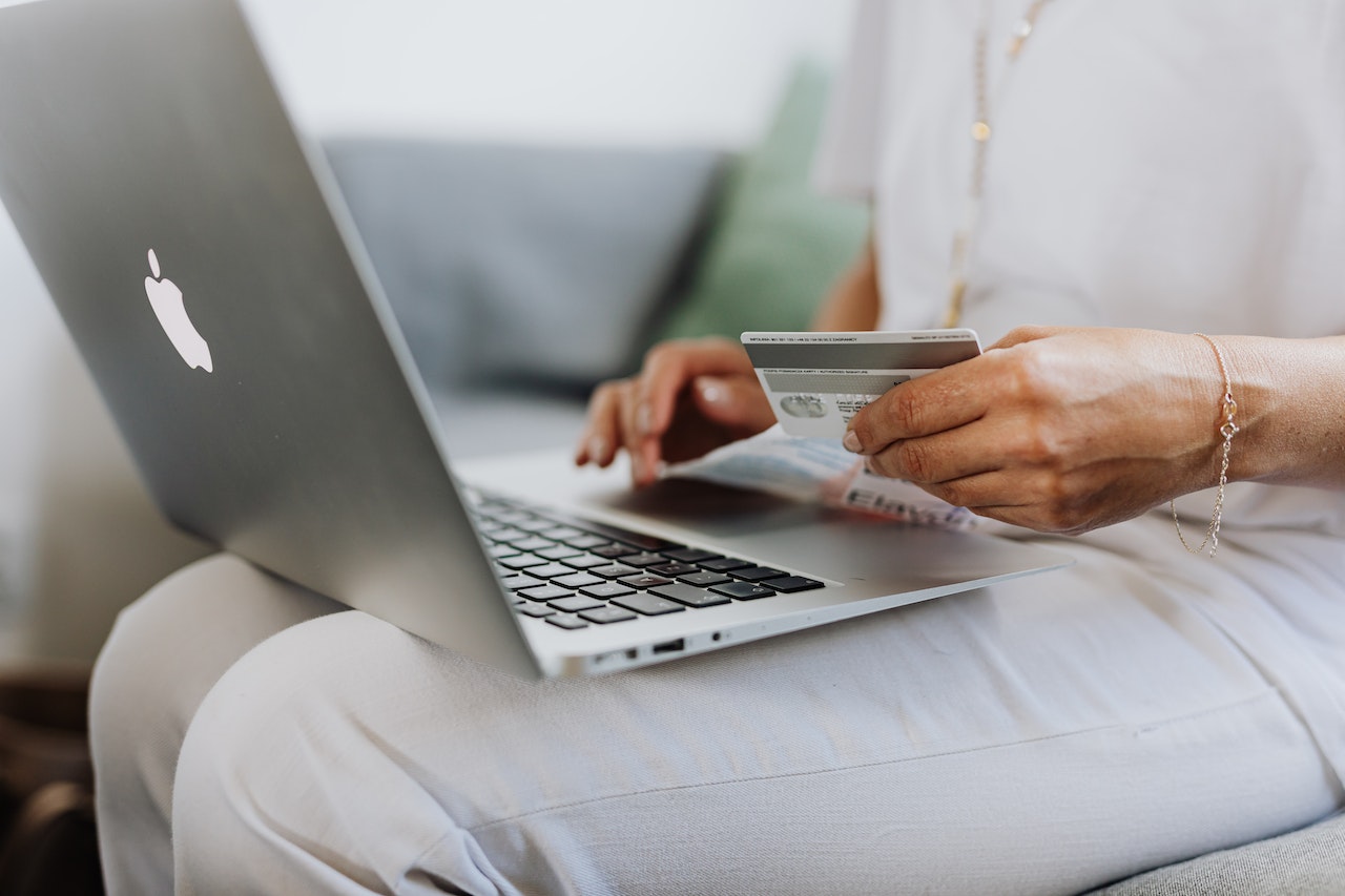Person holding a credit card while using a laptop, likely making an online purchase, focusing on hands and devices, ideal for a social media scheduler context | plannthat.com